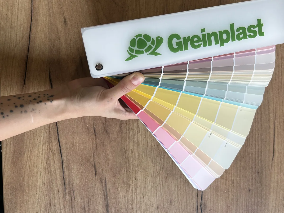 Dłoń trzymająca rozłożony wachlarz kolorów Greinplast nad blatem