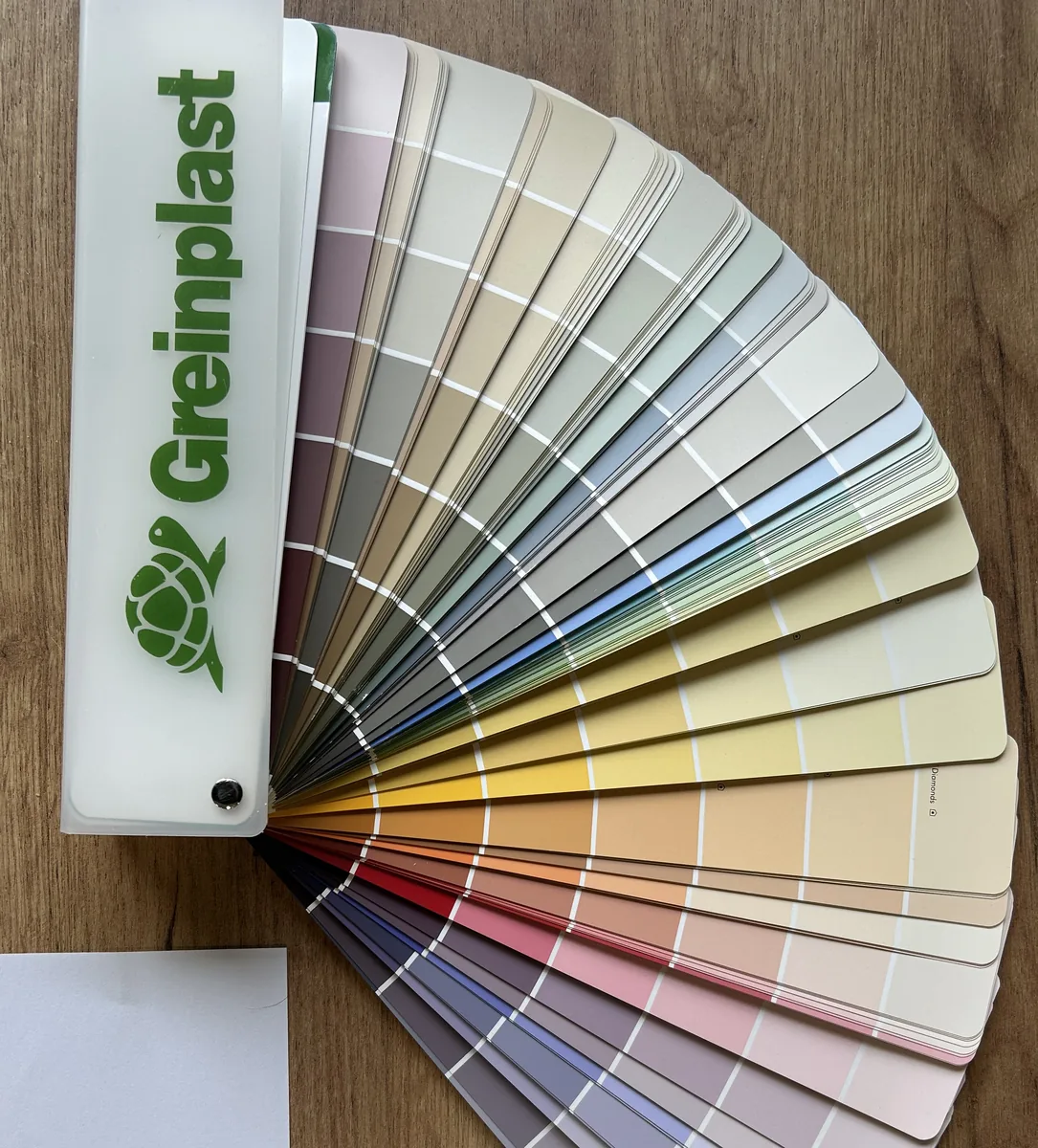 Rozłożony wachlarz z próbkami kolorów farb Greinplast leżący na drewnianym blacie